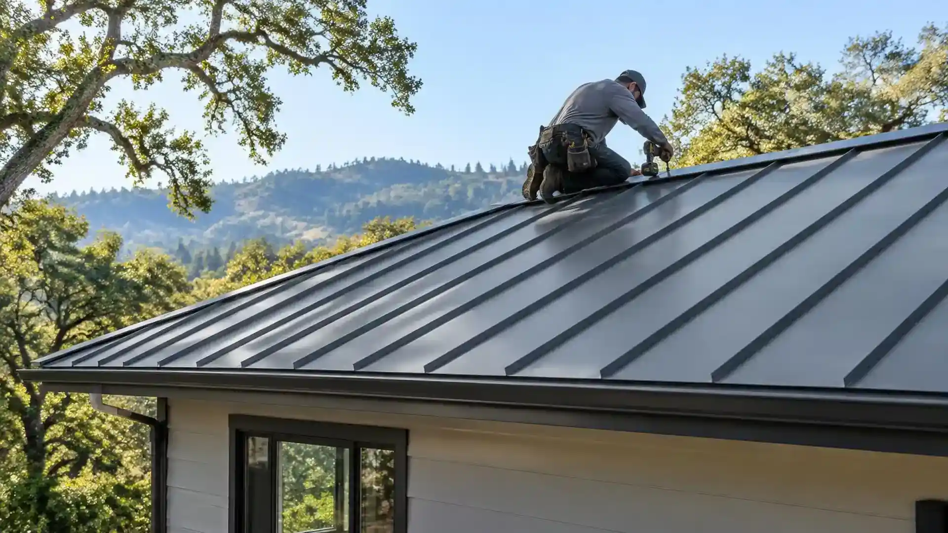 Roofer fastening a metal roof panel near the ridge.