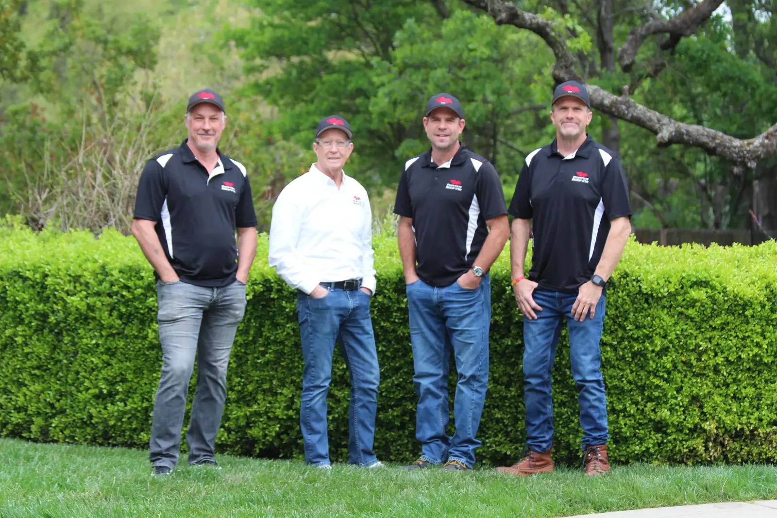 Four men in Porter Roofing shirts and caps standing in front of a green hedge.