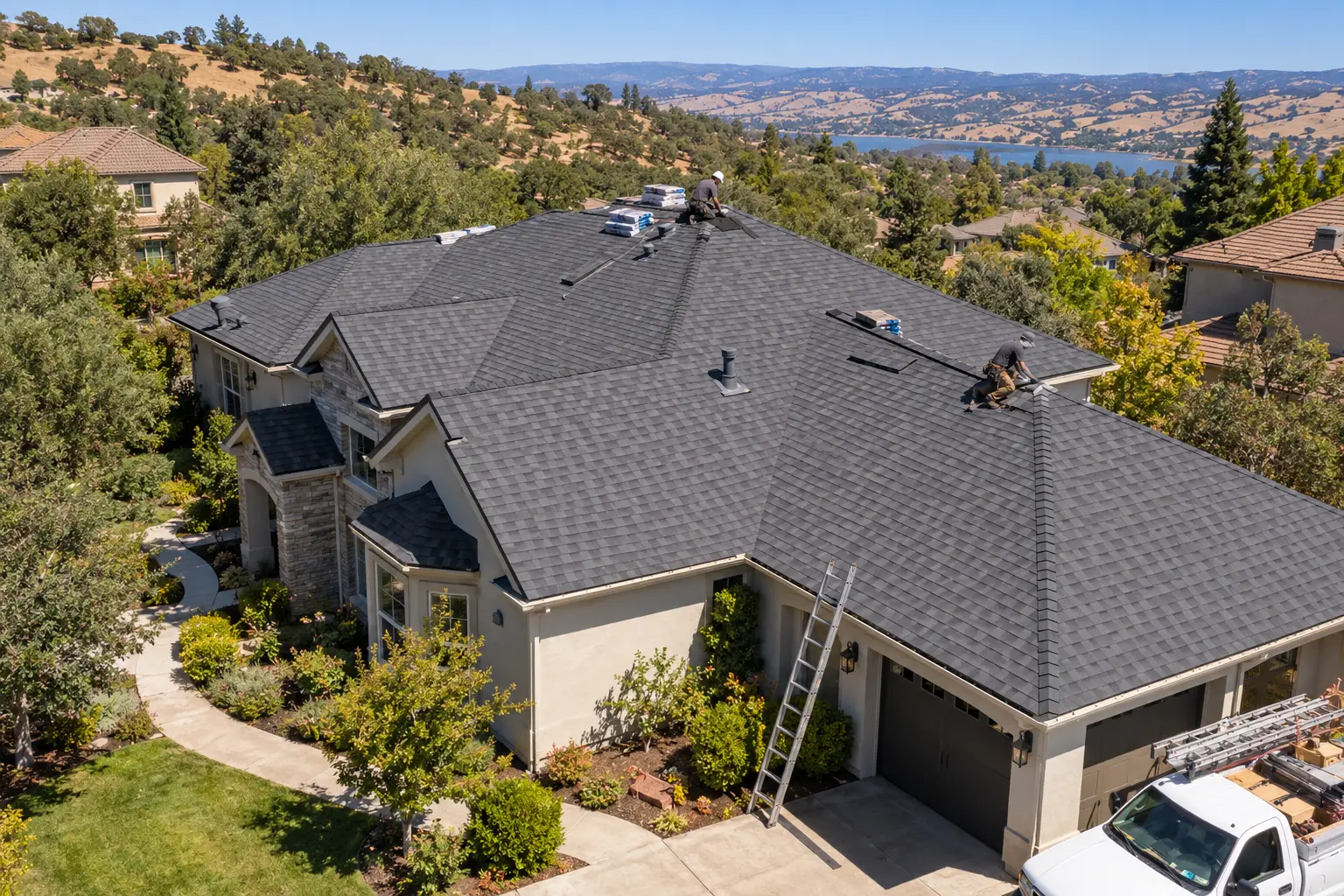 Two roofers installing dark gray shingles on a large home's roof