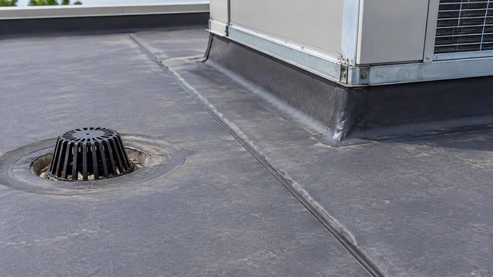 Roofer checking a flat commercial roof beside a rooftop unit.