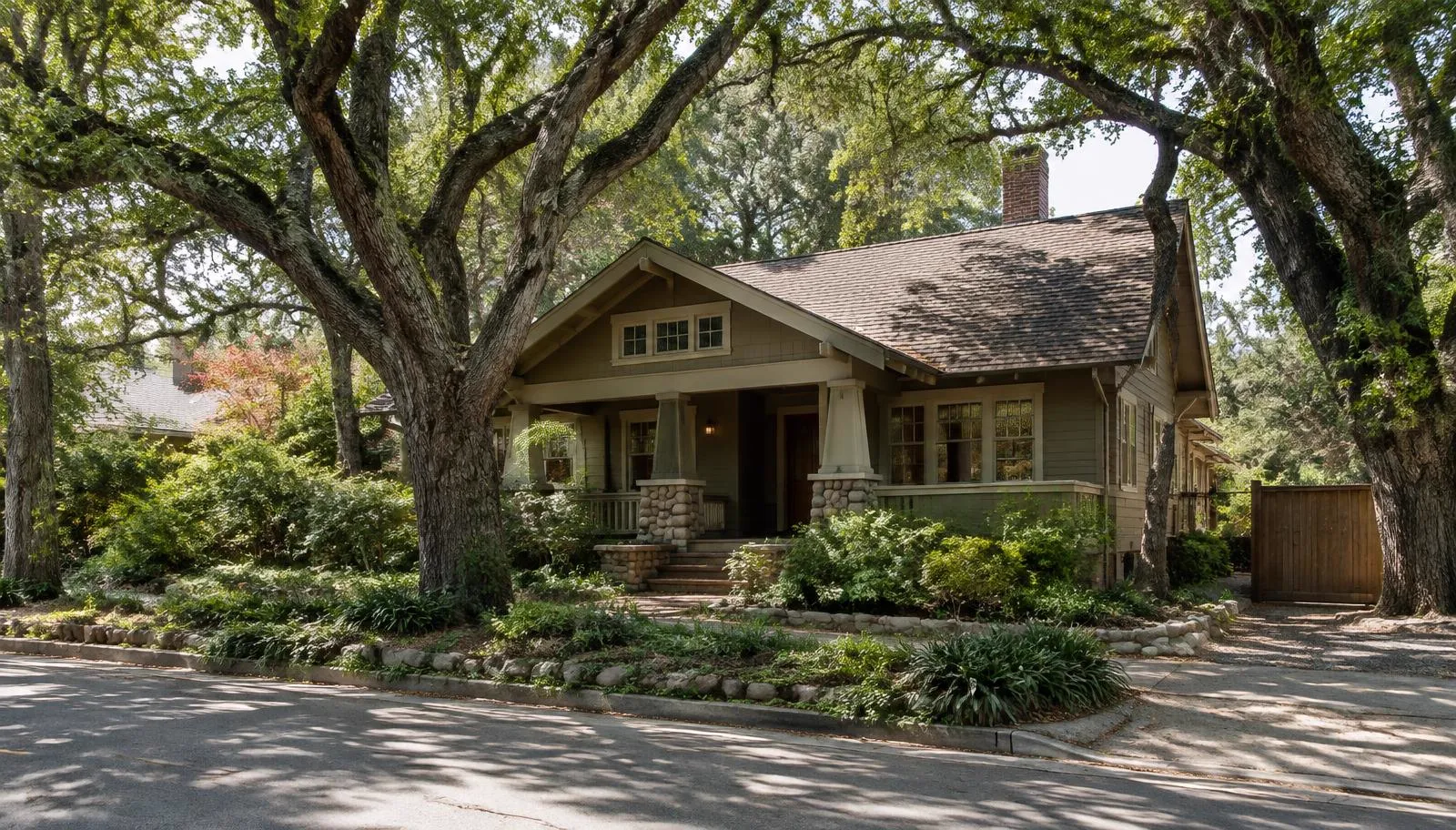 Craftsman home with a brown shingle roof under large oak trees.