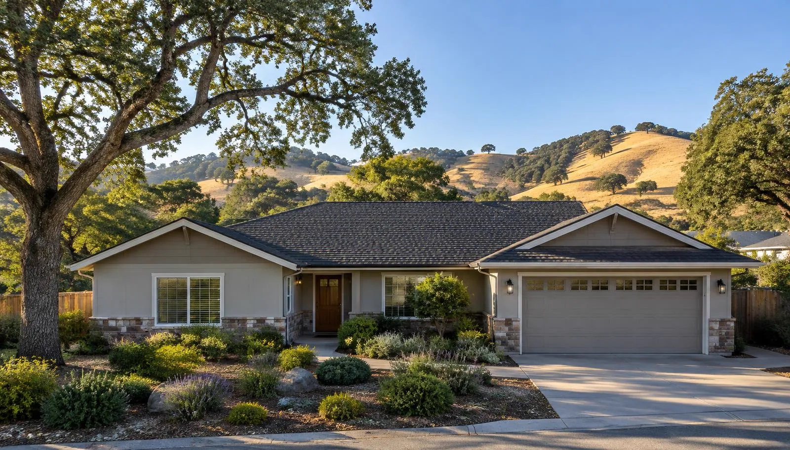 Single-story home with a charcoal shingle roof below golden oak-dotted hills.