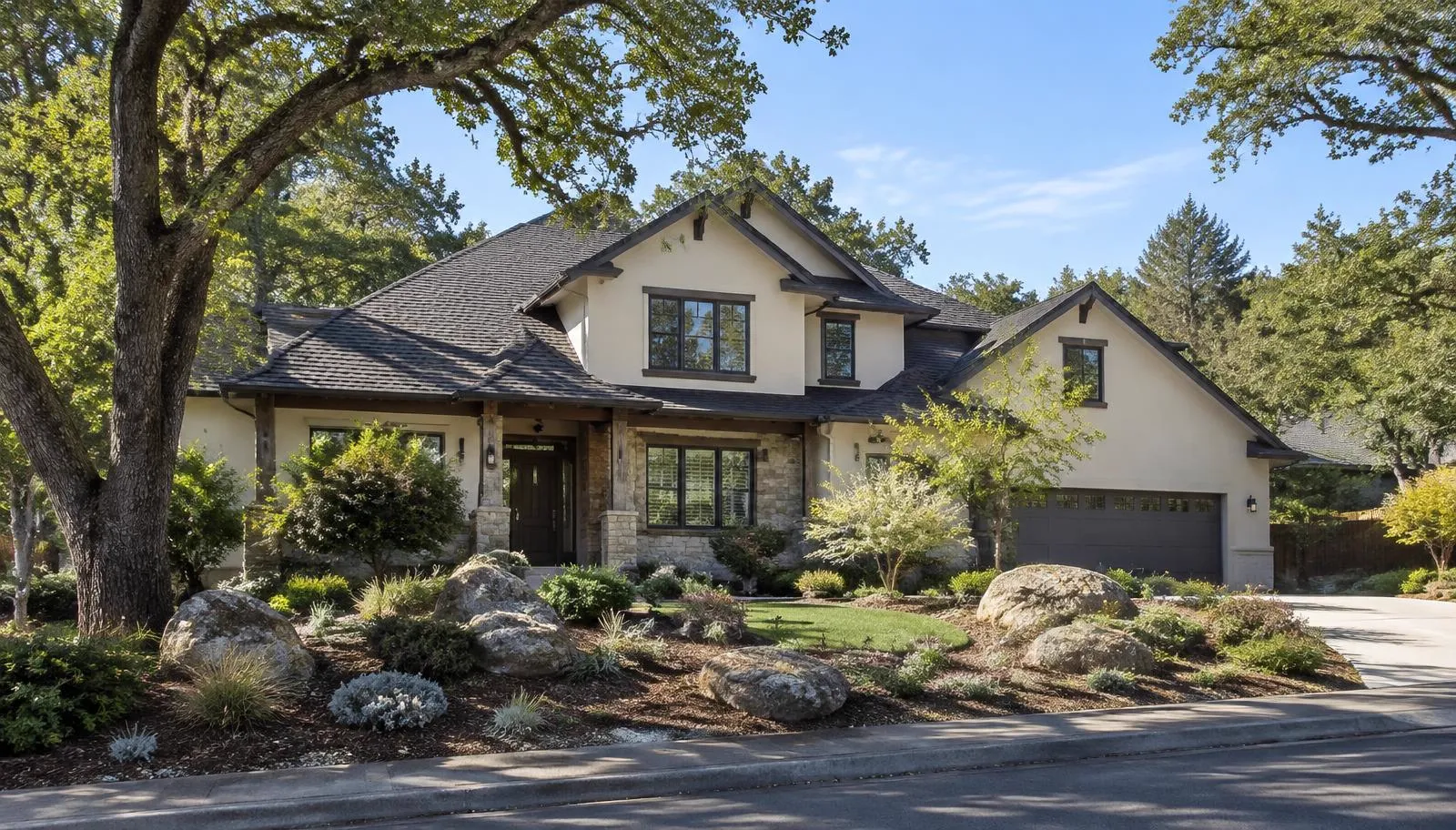 Two-story home with a dark shingle roof and boulders in the front yard.